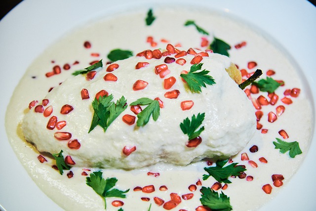 A poblano pepper covered in a white sauce and topped with pomegranate seeds and parsley.