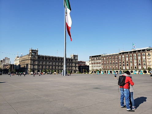 Zocalo in Mexico City with colonial buildings in the back and a giant Mexican flag in the middle.