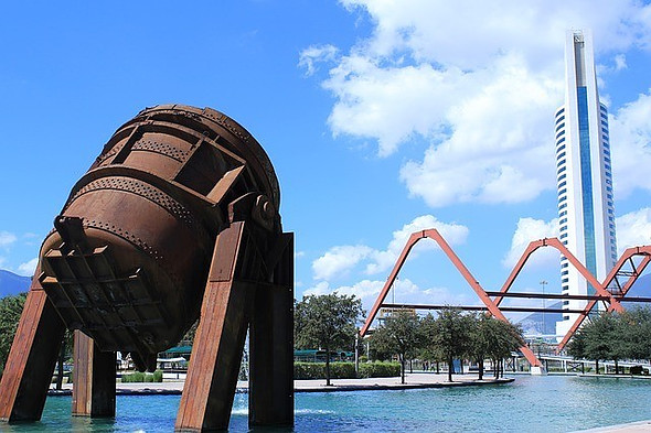 Artificial canal with a a close-up of a fountain and a red structure and tall building in the back.