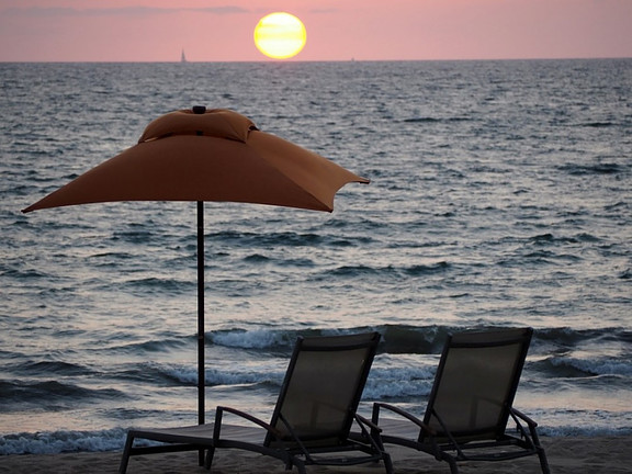 Two chairs and an umbrella with the sunset as backdrop.