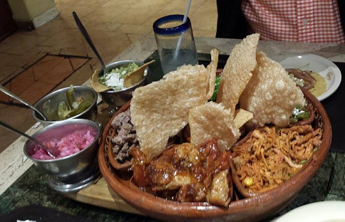 Plate with pork rinds, carnitas, shredded pork meat, guacamole, red onion and chili peppers.