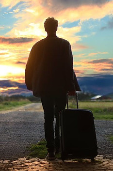 Man waking against the sun rolling his suitcase.