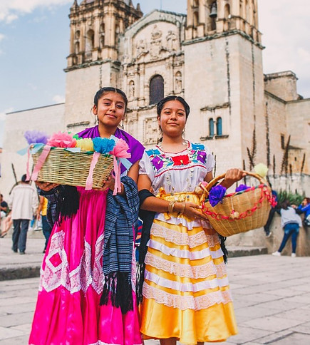 Two indigenous women wearing traditional clothes and carrying two baskets outside the Oaxaca Cathedral.