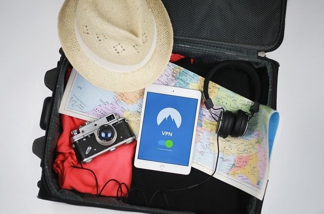 Open suitcase with clothes, a hat, a tablet, a map and a camera.