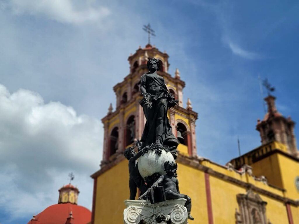 A closeup of a saint in front of a yellow basilica.