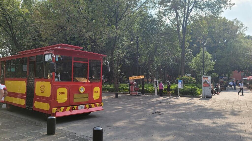 A red trolley in front of a plaza.