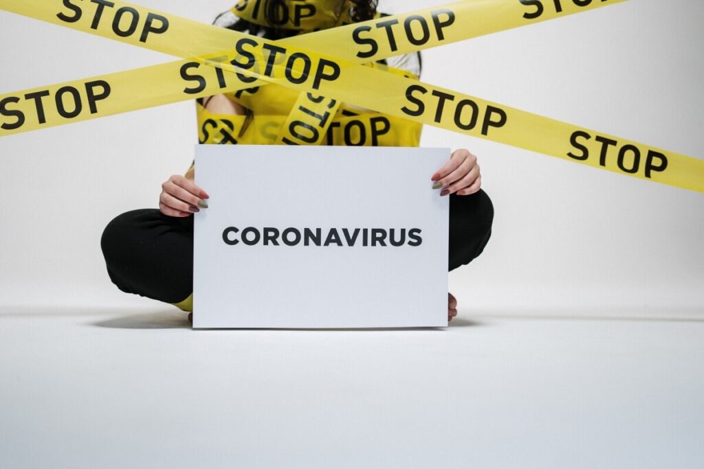 Woman holding a coronavirus sign surrounded by yellow tape reading stop