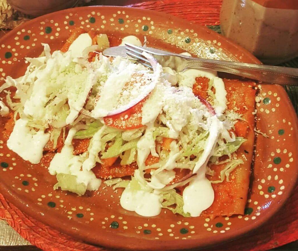 Enchiladas with lettuce, tomato, and cream.