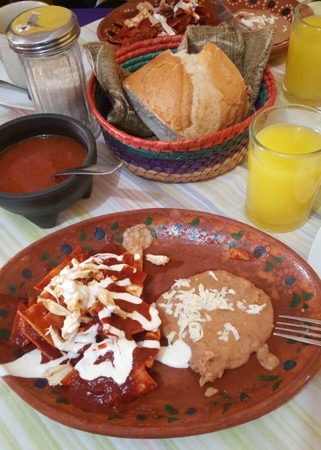 Chilaquiles rojos with cream, cheese, beans, and orange juice.