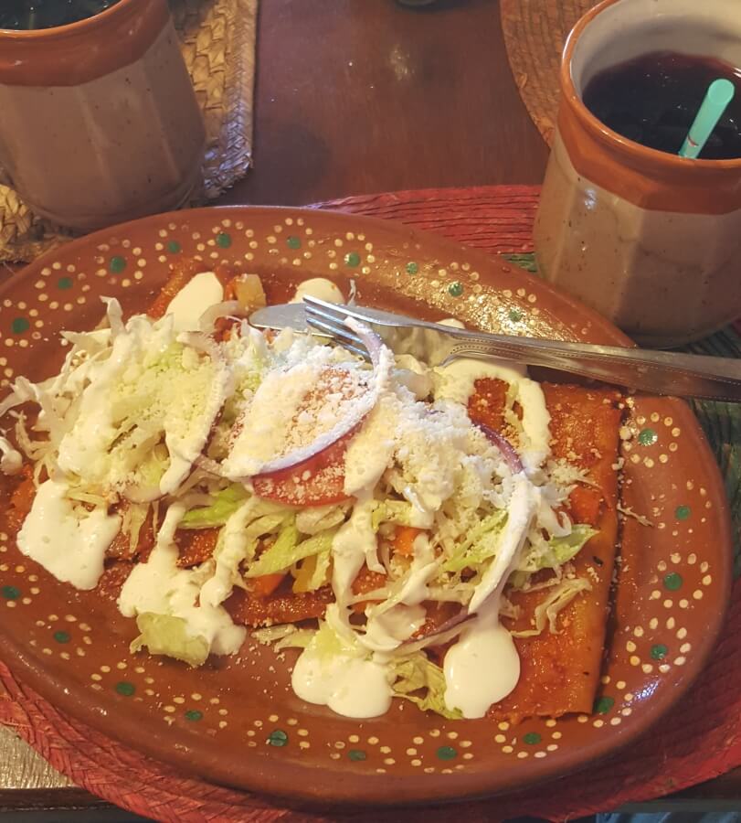 Enchiladas topped with queso fresco, lettuce, and cream.