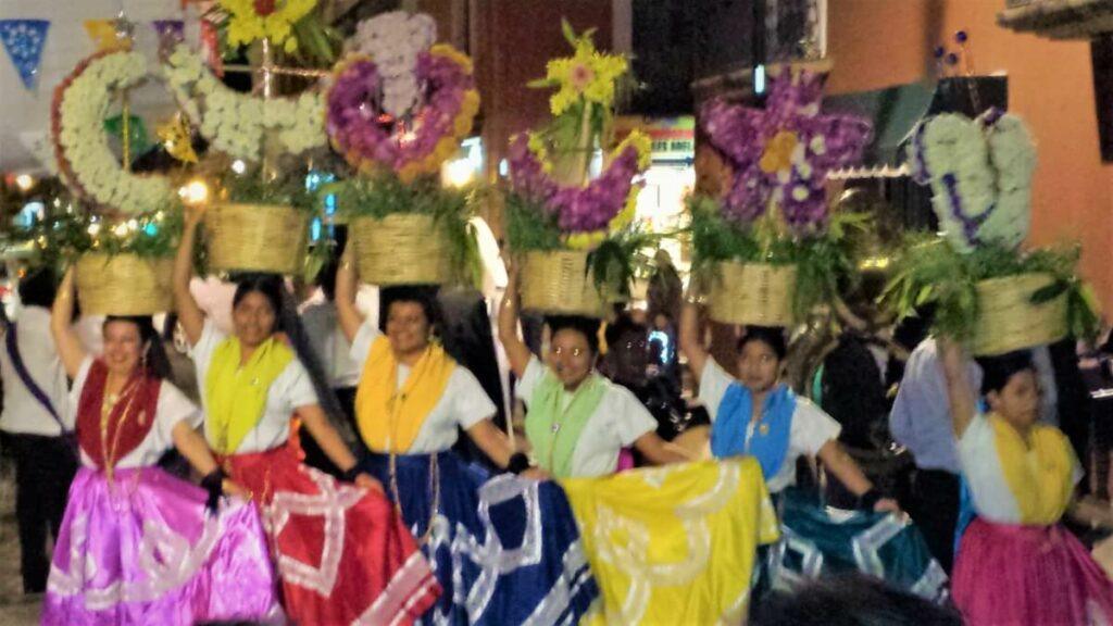 Various young women dressed in their regional costumes and holding baskets with flowers on their heads.
