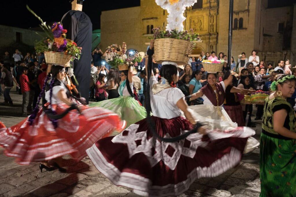 A group of women with traditional Oaxacan clothing carrying baskets and dancing.