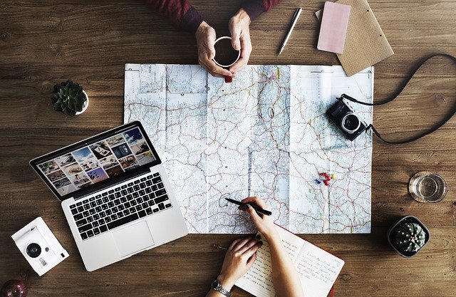 Two people planning a trip with a laptop, a notebook, and a map.