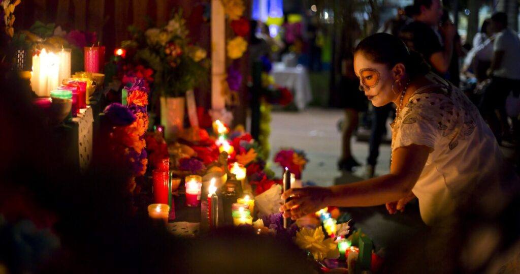 A woman before an ofrenda full of candles and flowers.