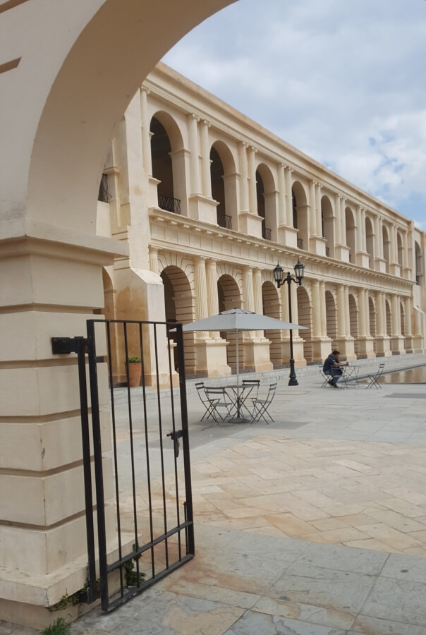 Colonial building with several arches and a couple of tables in front of it.