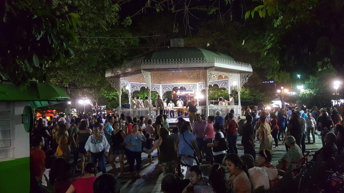 A crowd dancing around a green gazebo at night.