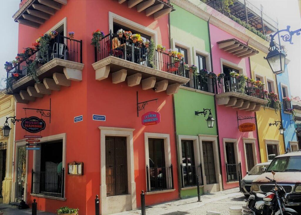 A colorful building painted in red, green, pink, yellow, and blue with balconies with flowrpots.