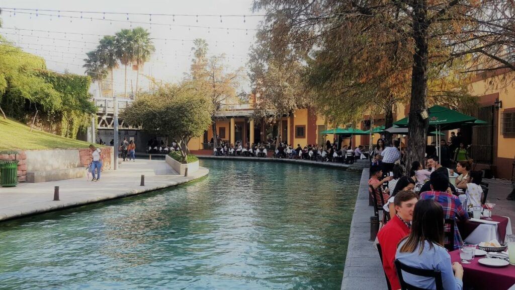 Several people eating at tables along an artificial river.