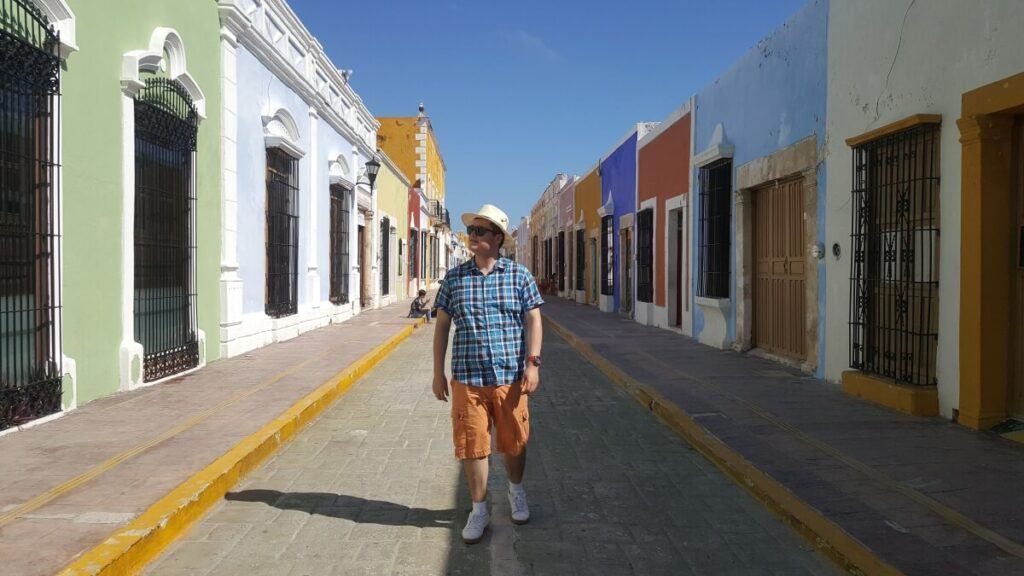 A young man walking in the middle of a colorful street.