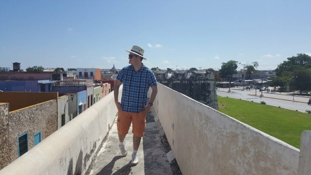 A young man dressed in a blue shirt and orange shorts walking on top of a wall.