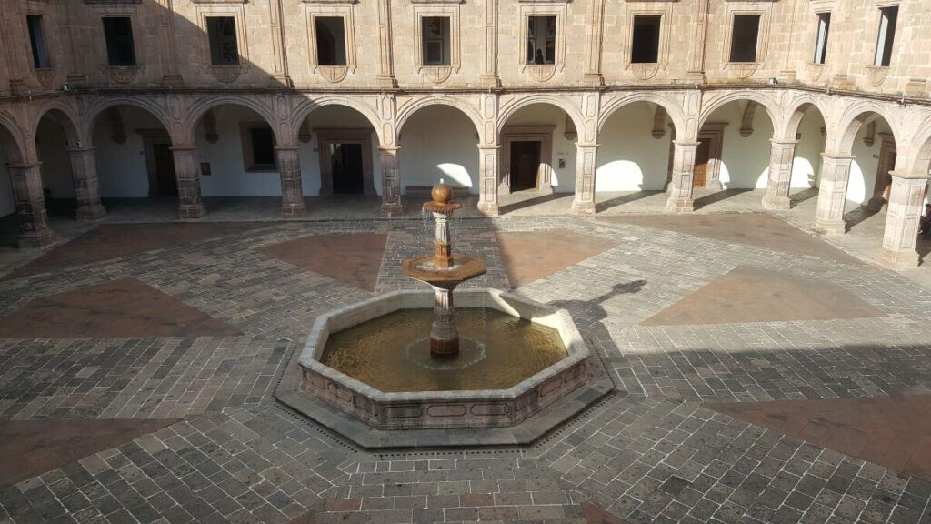 A large patio with arches and a fountain in the middle.