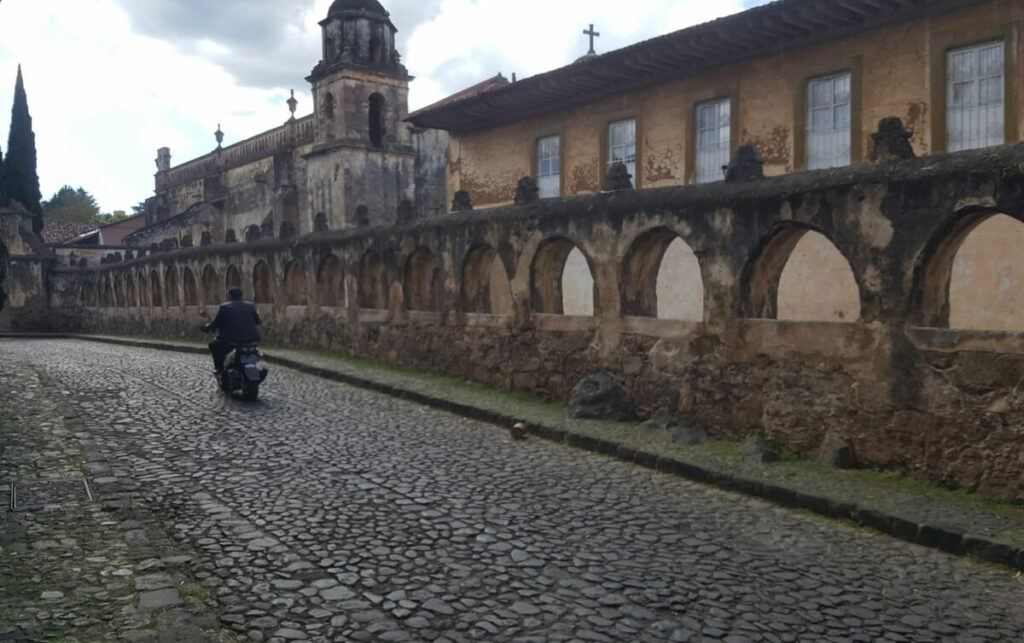 A biker passing by a church with an arched fence.