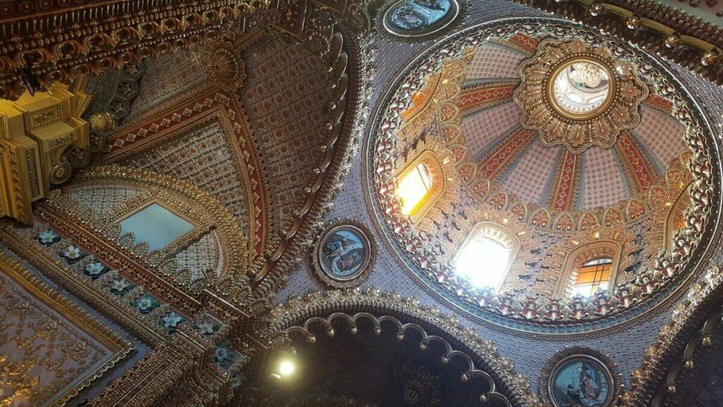 Interior of a church dome decorated in red, pink, and gold tones.