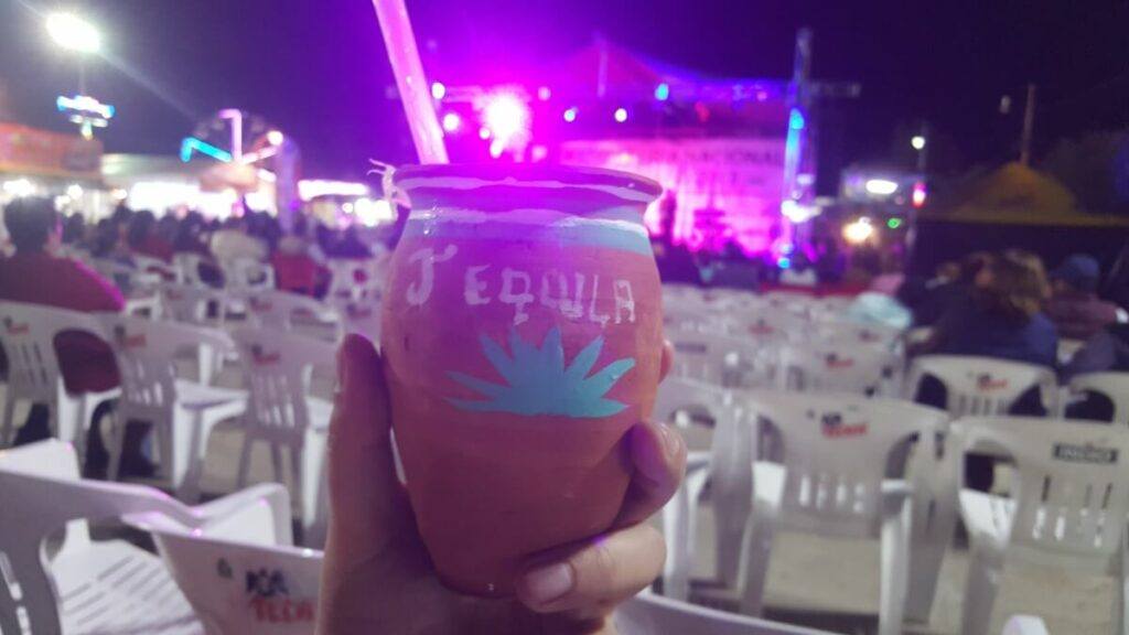 A hand holding a clay glass with tequila.