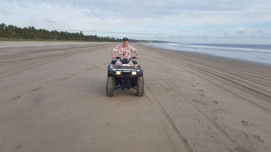 A young man riding an ATV at the beach.